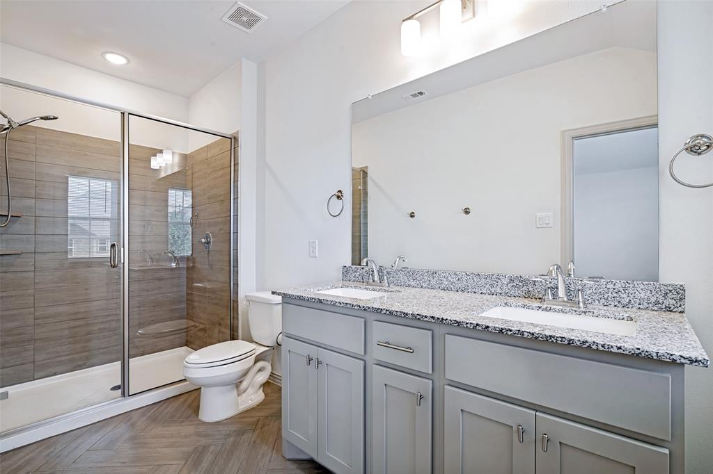 1006 Emil Place Allen, TX 75013 - Photo 16 of 28 Contemporary bathroom featuring a spacious glass-enclosed shower with horizontal tile work, a dual vanity with light gray cabinetry, and a speckled countertop