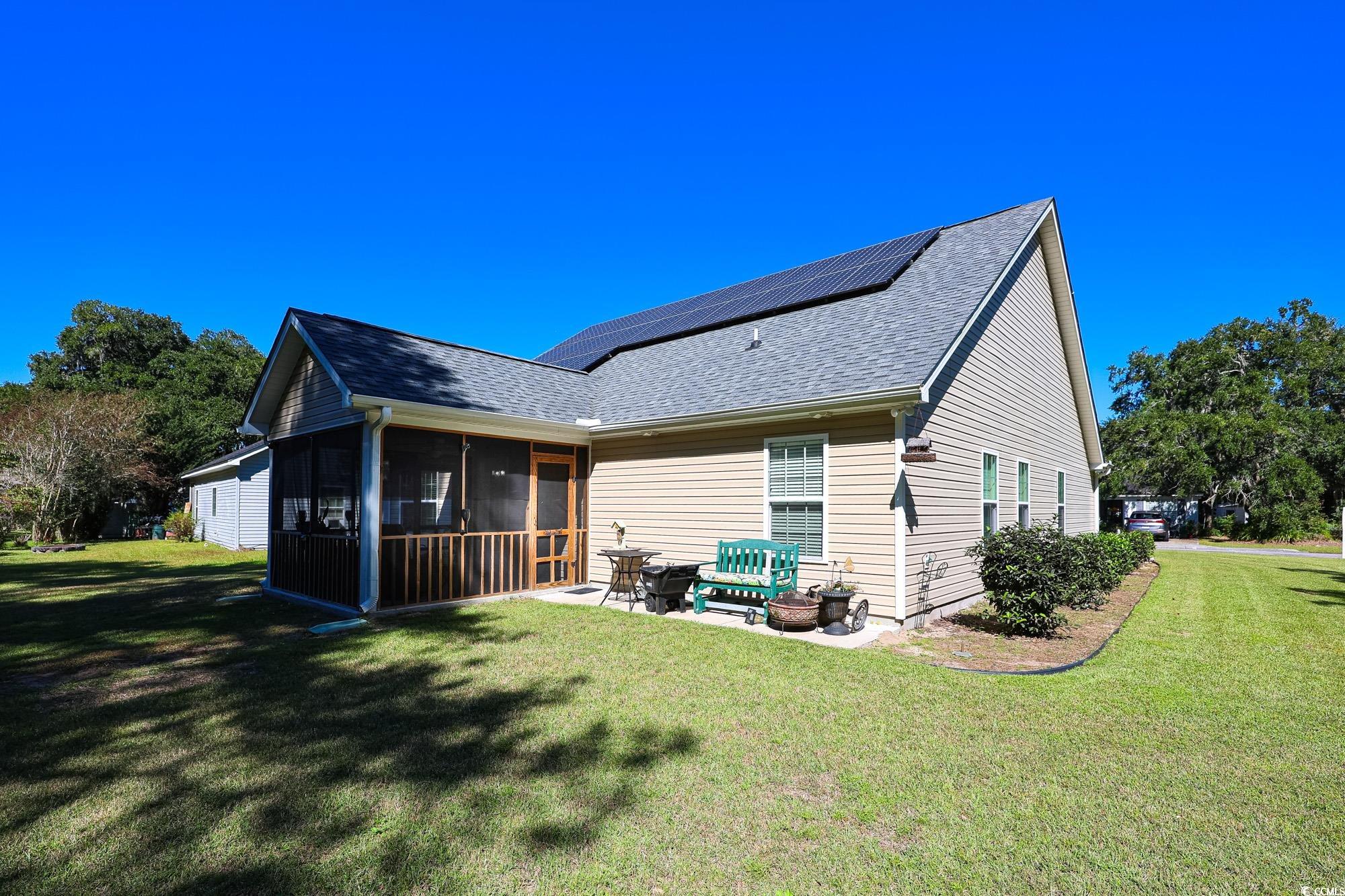 13 Daniel Morrall Lane Georgetown, SC 29440 - Photo 27 of 30 Rear view of house featuring a sunroom, a yard, roof with shingles, and roof mounted solar panels