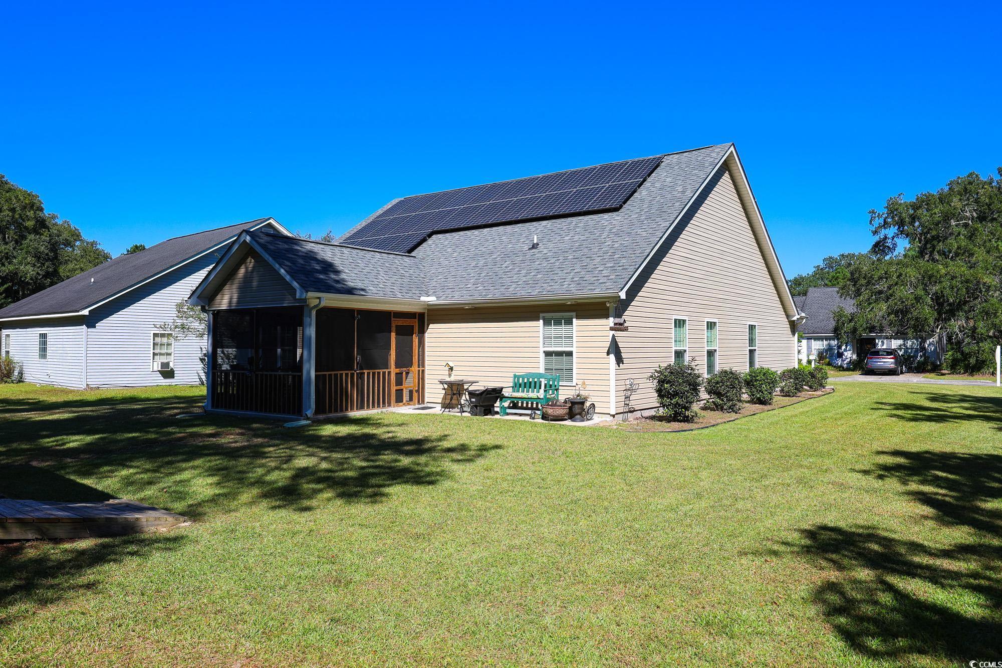 13 Daniel Morrall Lane Georgetown, SC 29440 - Photo 28 of 30 Back of property with a sunroom, solar panels, roof with shingles, a yard, and a patio