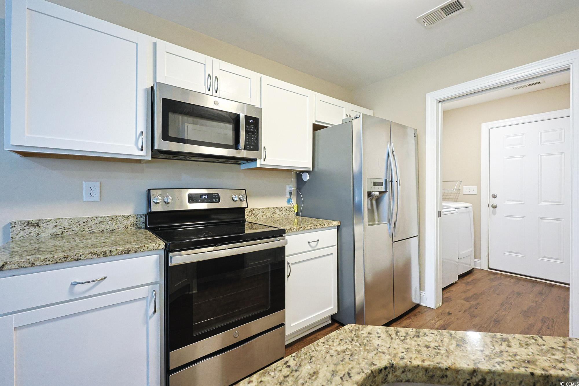 13 Daniel Morrall Lane Georgetown, SC 29440 - Photo 8 of 30 Kitchen featuring appliances with stainless steel finishes, white cabinetry, dark wood-style flooring, and light stone counters