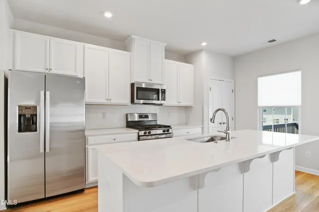 a kitchen with stainless steel appliances granite countertop a refrigerator a stove top oven a dining table and chairs with wooden floor