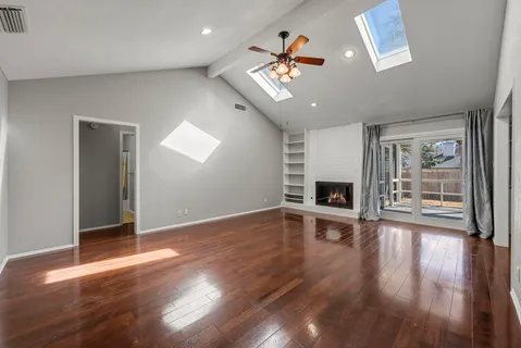an empty room with wooden floor fireplace and windows