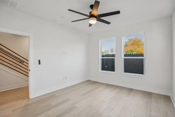 an empty room with wooden floor fan and windows