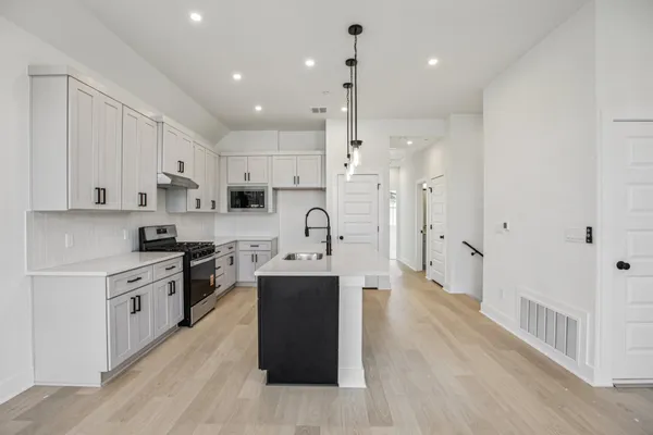 a large kitchen with stainless steel appliances kitchen island granite countertop a stove a sink a refrigerator and white cabinets with wooden floor