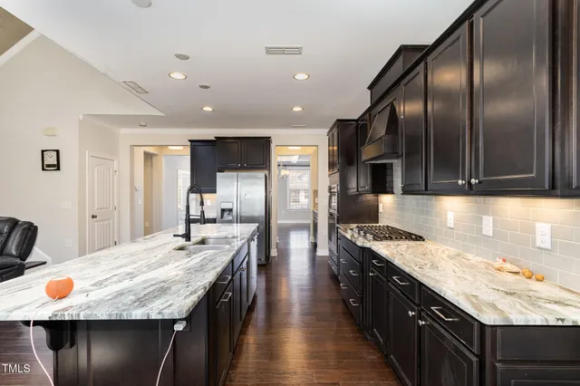 a kitchen with stainless steel appliances granite countertop a refrigerator a oven a sink with wooden cabinets and wooden floor