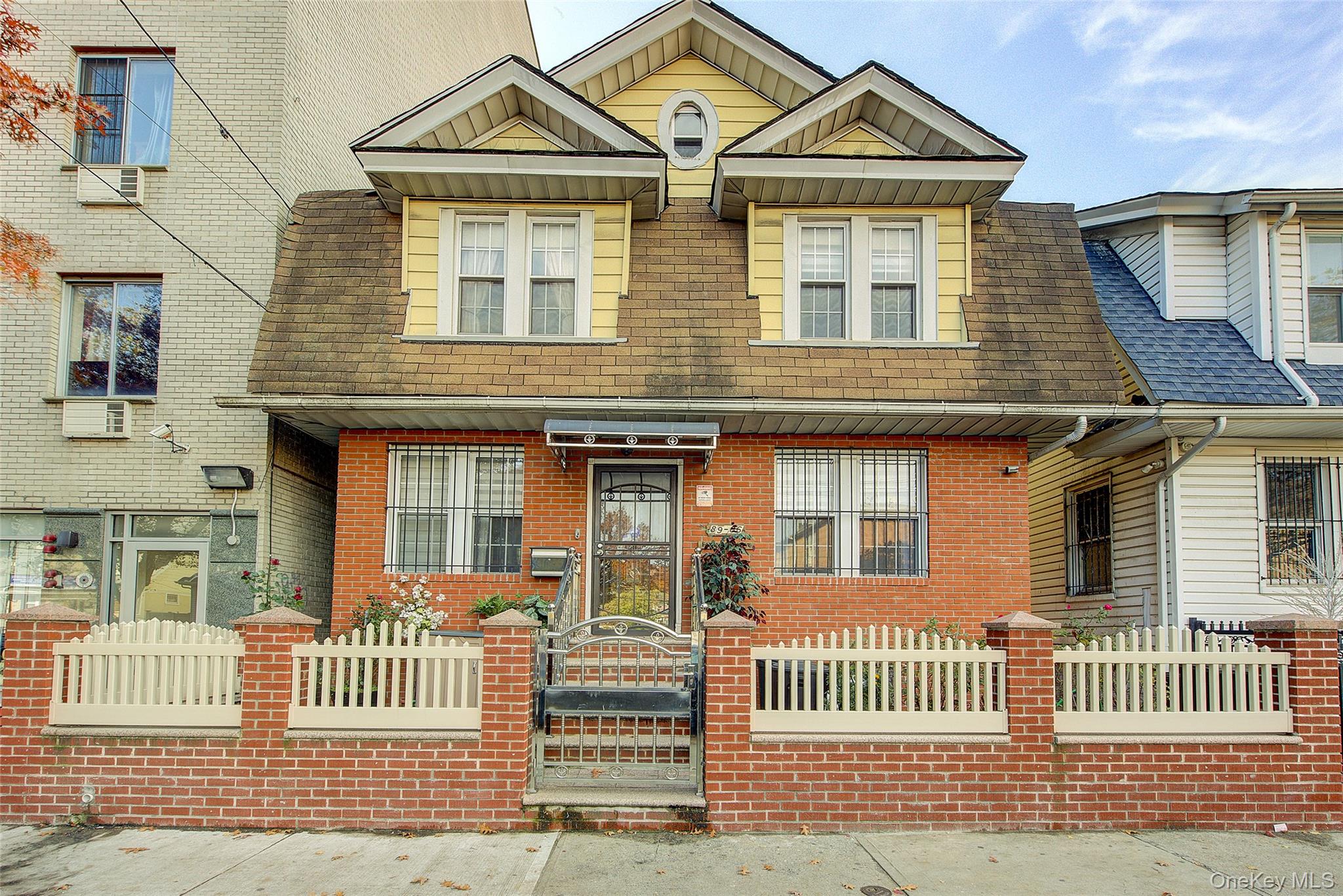 View of front facade featuring a fenced front yard, a shingled roof, brick siding, and a gate