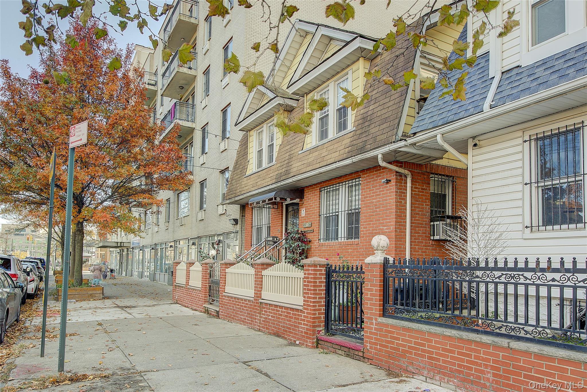 89-06 175th Street Queens, NY 11432 - Photo 2 of 29 View of property exterior featuring roof with shingles, a fenced front yard, brick siding, and mansard roof