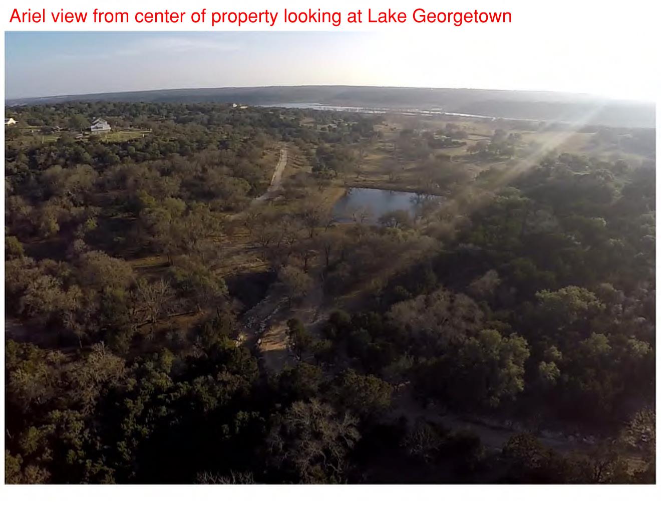 242 Landons Way Georgetown, TX 78633 - Photo 28 of 30 An aerial panorama reveals a private pond nestled amidst verdant natural landscaping, with distant water views.