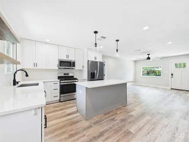 a kitchen with stainless steel appliances a refrigerator stove and white cabinets with wooden floor