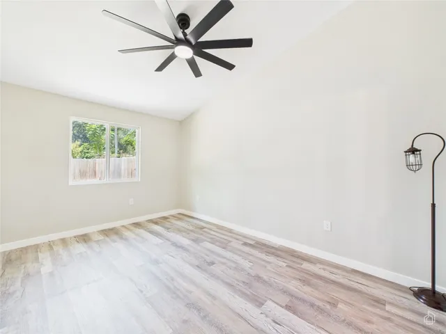 an empty room with wooden floor fan and windows
