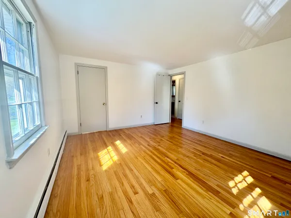a view of an empty room with wooden floor and a window