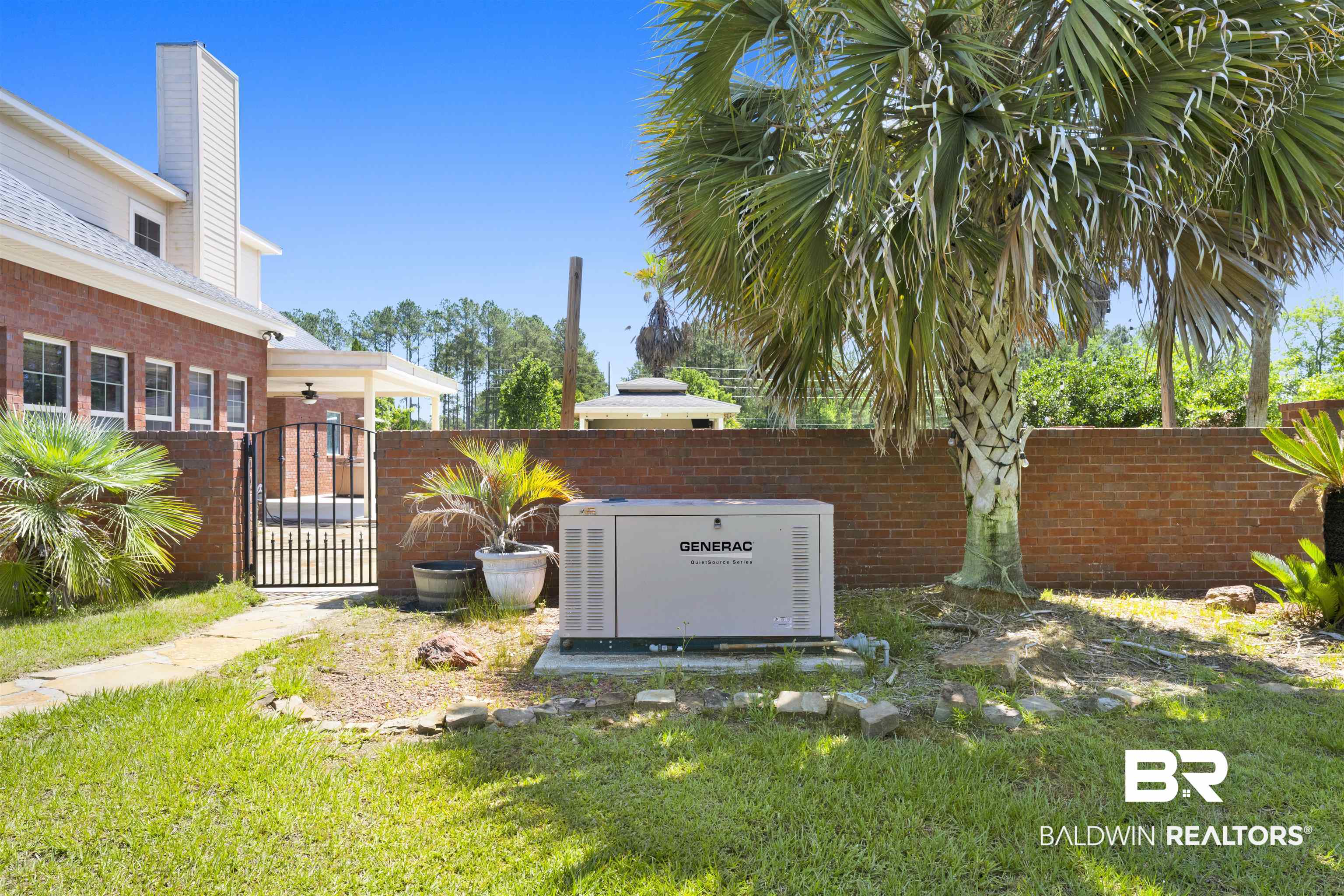 12944 Anna's Way Stapleton, AL 36578 - Photo 21 of 64 Whole-home generator on a concrete pad, surrounded by a brick privacy wall and mature palm trees