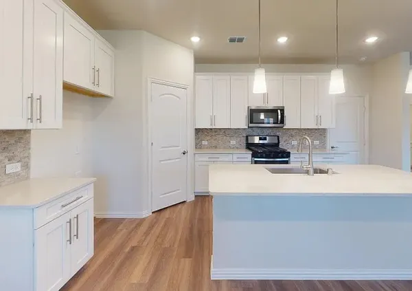 a kitchen with stainless steel appliances granite countertop a sink a stove a refrigerator and white cabinets with wooden floor