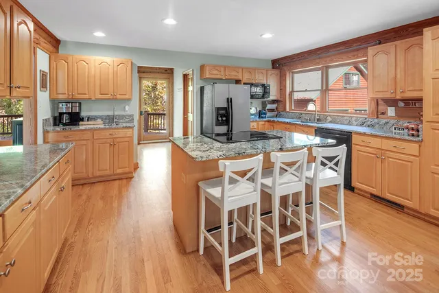 a kitchen with stainless steel appliances kitchen island granite countertop a stove a refrigerator a sink a dining table and chairs with wooden floor
