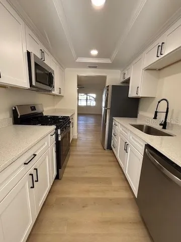 a kitchen with stainless steel appliances a sink dishwasher a stove top oven a refrigerator with wooden floor and cabinets