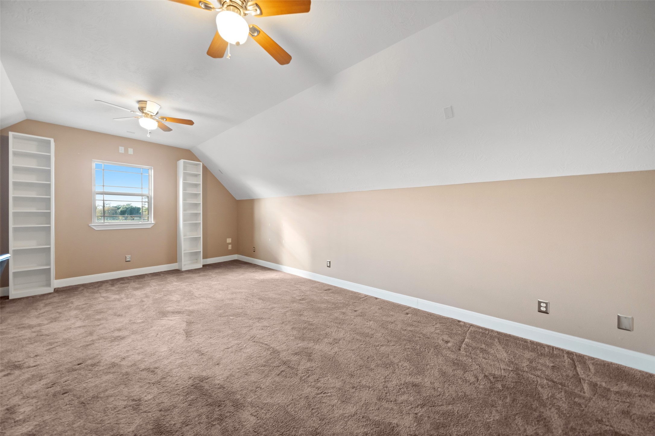 26752 Nelson Road Hempstead, TX 77445 - Photo 31 of 45 Spacious upstairs bonus room features soft carpet, sloped ceilings, ceiling fans, and built-in shelving, providing flexible living or workspace options.
