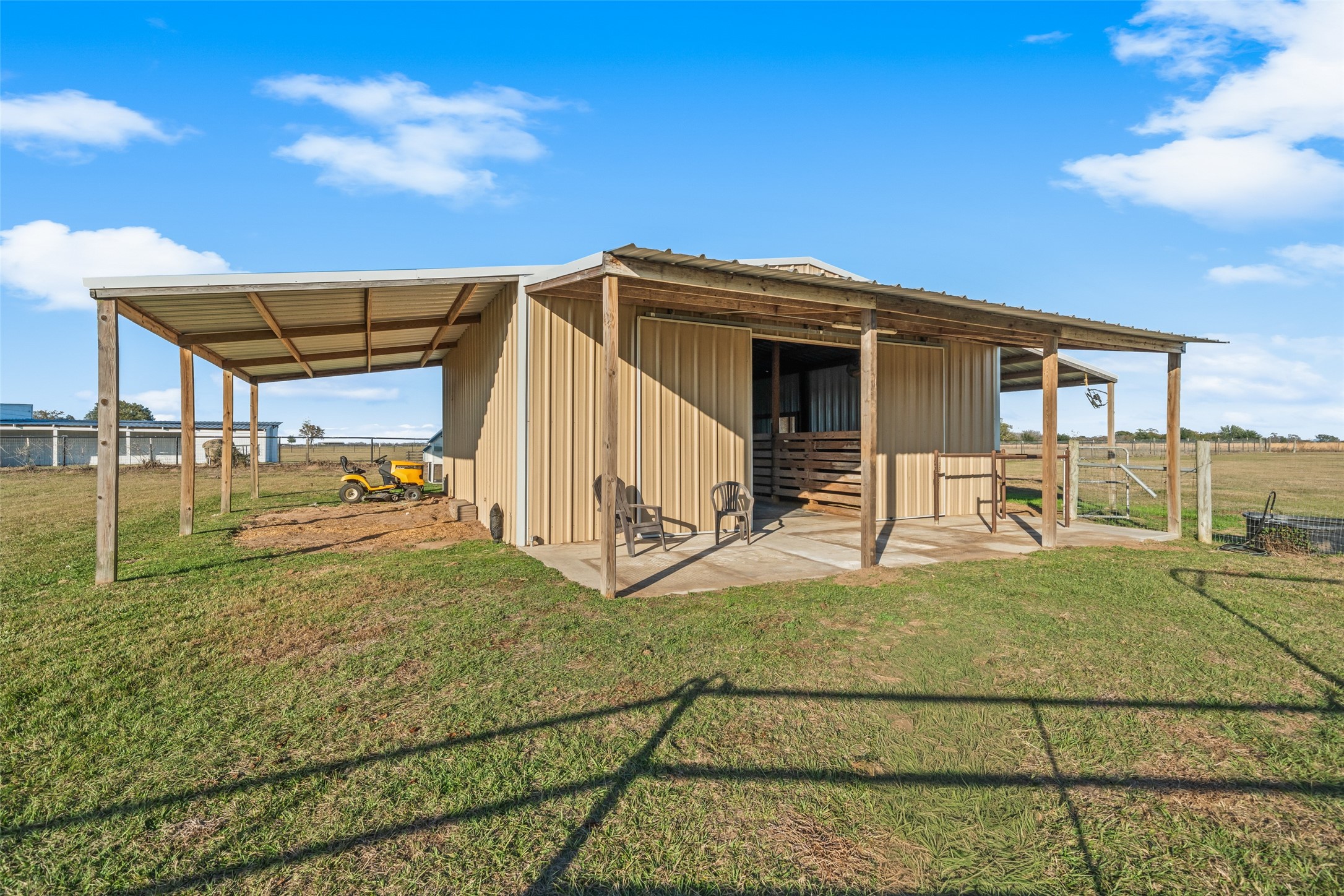 26752 Nelson Road Hempstead, TX 77445 - Photo 37 of 45 Metal barn features enclosed stall areas with extended covered overhangs on each side, offering shade, storage, and flexible livestock use.