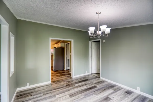 an empty room with wooden floor chandelier and windows