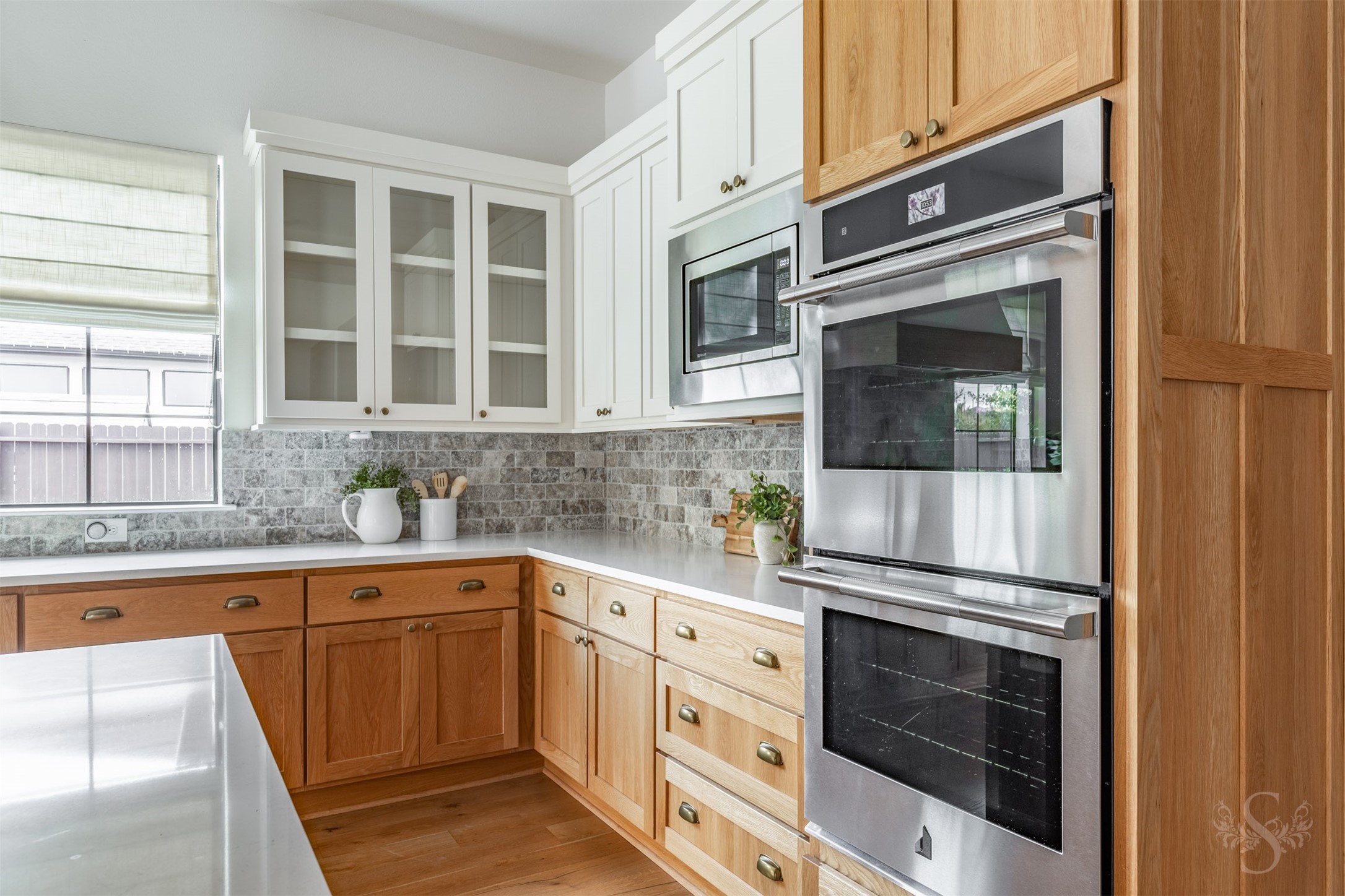 27919 Indigo Ridge Drive Fulshear, TX 77441 - Photo 20 of 50 This stylish kitchen features double ovens, crisp white upper cabinetry with glass fronts, and warm lower cabinets that create a beautiful blend of style and contrast. A classic brick-pattern backsplash and generous counter space make this area ideal for cooking, baking, and effortless meal prep.