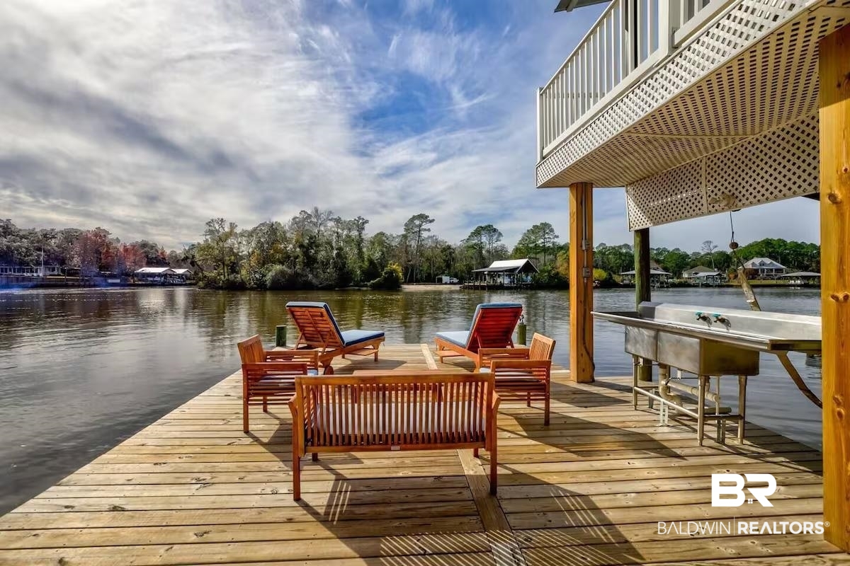 16297 Honey Road Summerdale, AL 36580 - Photo 23 of 24 Expansive wooden deck with water frontage, featuring an outdoor utility sink, and a balcony with white lattice detailing