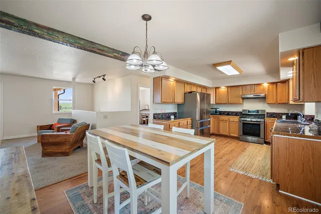 a kitchen with stainless steel appliances kitchen island granite countertop a stove a sink a dining table and chairs with wooden floor