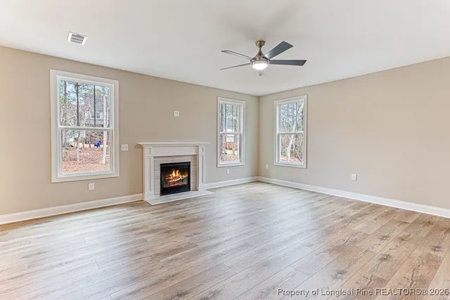 a view of an empty room with wooden floor fireplace and a window