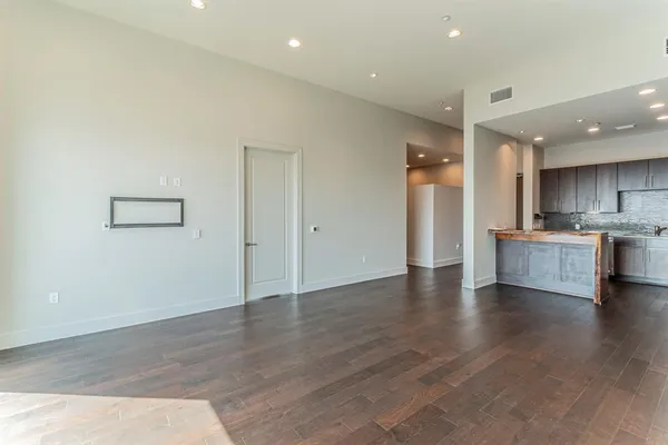 an empty room with wooden floor and a kitchen