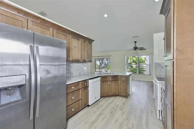 a kitchen with stainless steel appliances granite countertop a refrigerator a sink dishwasher a stove and white countertops with wooden floor