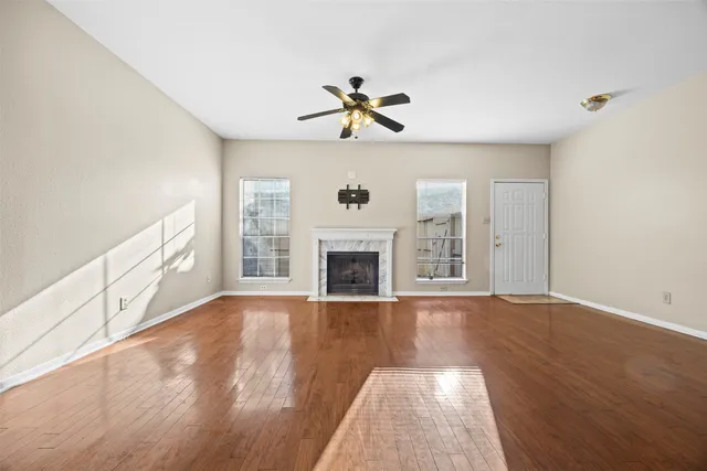 a view of a livingroom with a fireplace a ceiling fan and wooden floor