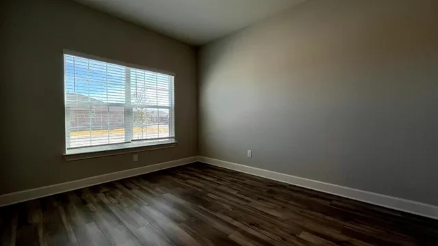 an empty room with wooden floor ceiling fan and windows