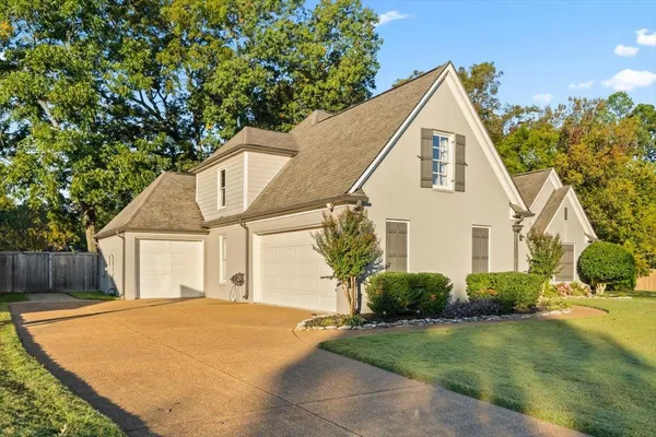 a view of a white house next to a yard with a large tree