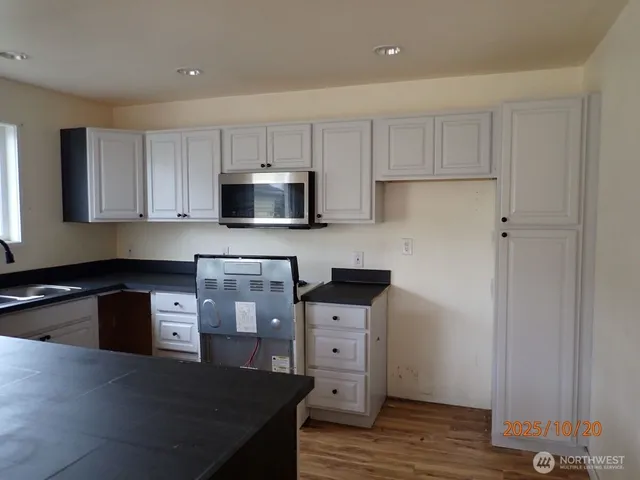 a kitchen with granite countertop a stove top oven a sink dishwasher and white cabinets with wooden floor