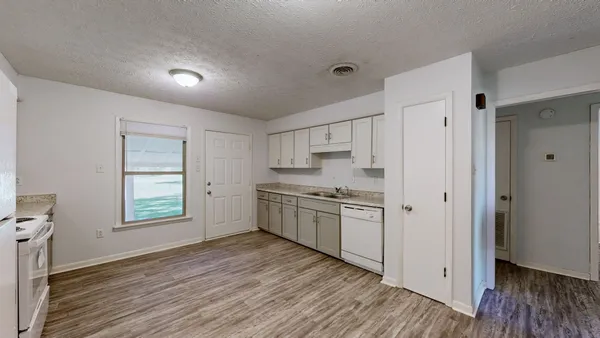 a kitchen with stainless steel appliances granite countertop a refrigerator a sink dishwasher a stove and white countertops with wooden floor