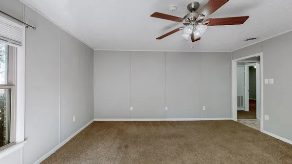 an empty room with a chandelier fan and windows