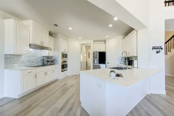 a large kitchen with stainless steel appliances refrigerator a microwave oven stove and white cabinets with wooden floor