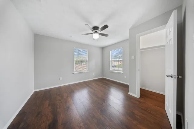 an empty room with wooden floor ceiling fan and windows