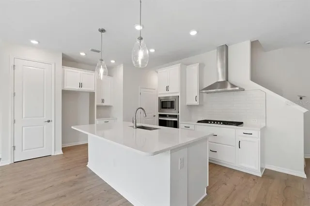 a kitchen with stainless steel appliances kitchen island granite countertop a stove a sink a refrigerator and white cabinets with wooden floor