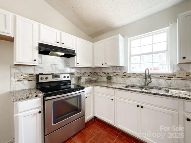 a kitchen with granite countertop white cabinets appliances a sink and a window