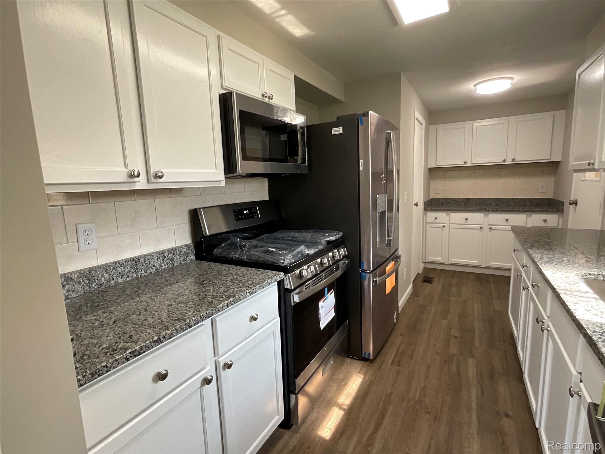 10119 Godfrey Road Bancroft, MI 48414 - Photo 10 of 47 Galley kitchen featuring white cabinetry with brushed nickel hardware, granite countertops, black gas range with stainless steel microwave, stainless steel refrigerator, and wood-finish flooring throughout
