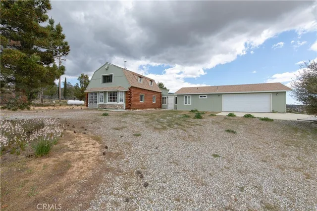 a front view of a house with a dirt yard and a large tree