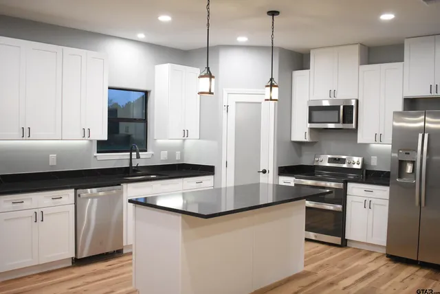 a kitchen with stainless steel appliances granite countertop a sink a stove a refrigerator and island with wooden floor