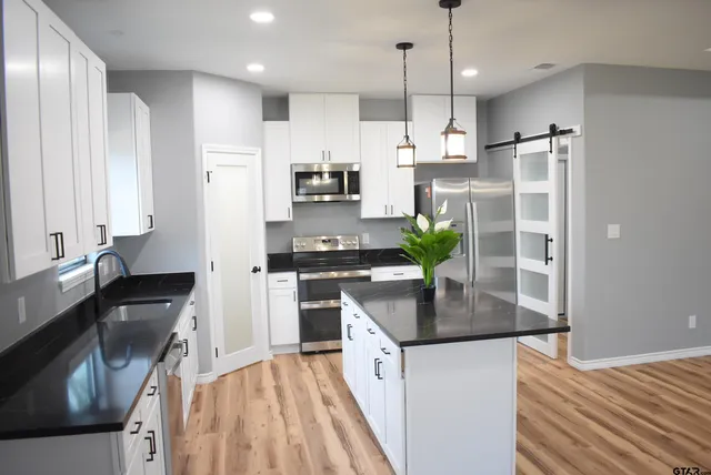 a kitchen with stainless steel appliances granite countertop a refrigerator a sink dishwasher a stove and white countertops with wooden floor