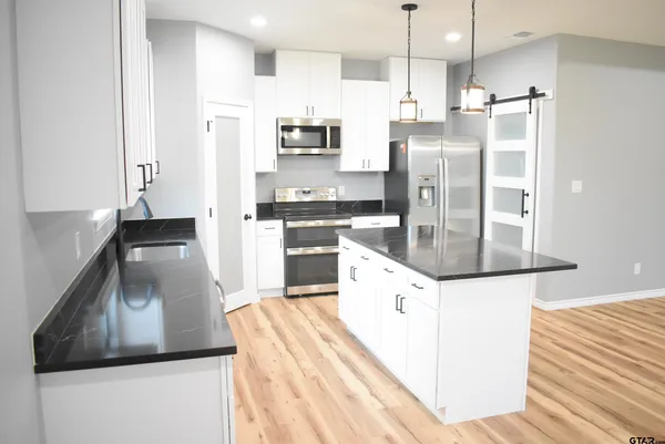 a kitchen with stainless steel appliances kitchen island granite countertop a refrigerator a stove and a sink with wooden floor