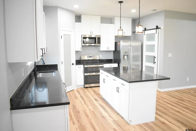 a kitchen with stainless steel appliances kitchen island granite countertop a refrigerator a stove and a sink with wooden floor