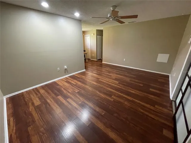 an empty room with wooden floor fan and windows