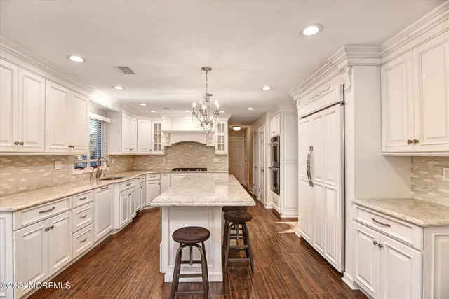 a kitchen with stainless steel appliances kitchen island granite countertop a refrigerator a sink dishwasher a stove and white cabinets with wooden floor