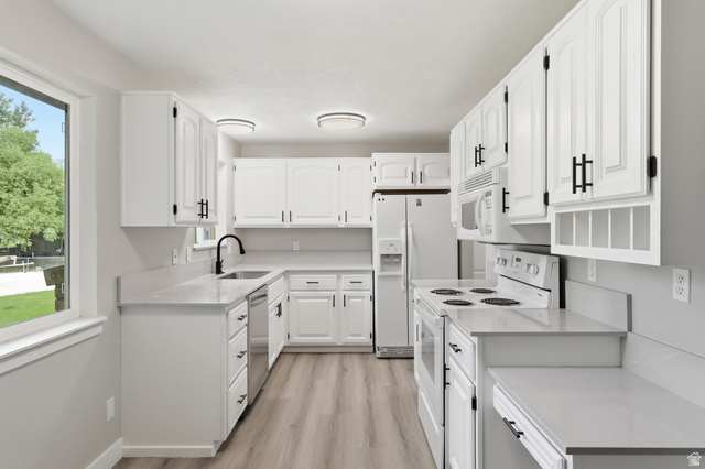 629 King Circle Layton, UT 84041 - Photo 4 of 26 Kitchen featuring white cabinetry with matte black hardware, light-toned countertops, stainless steel sink with a black gooseneck faucet, light wood-finish flooring, and a window overlooking exterior greenery