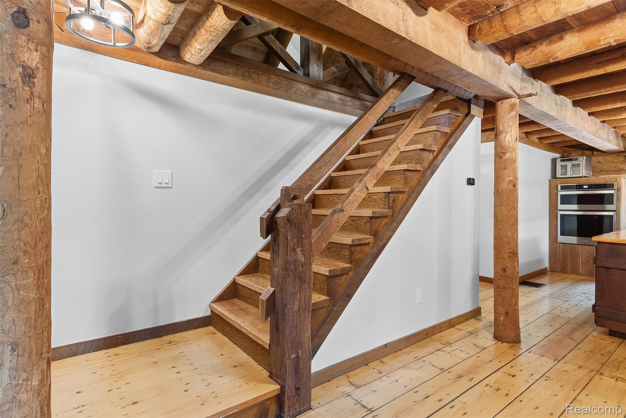 3656 Stanley Road Columbiaville, MI 48421 - Photo 23 of 65 Rustic wood staircase featuring a robust newel post and balustrade, complemented by exposed wood beams and wood-finish flooring