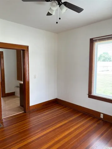 an empty room with wooden floor chandelier fan and windows