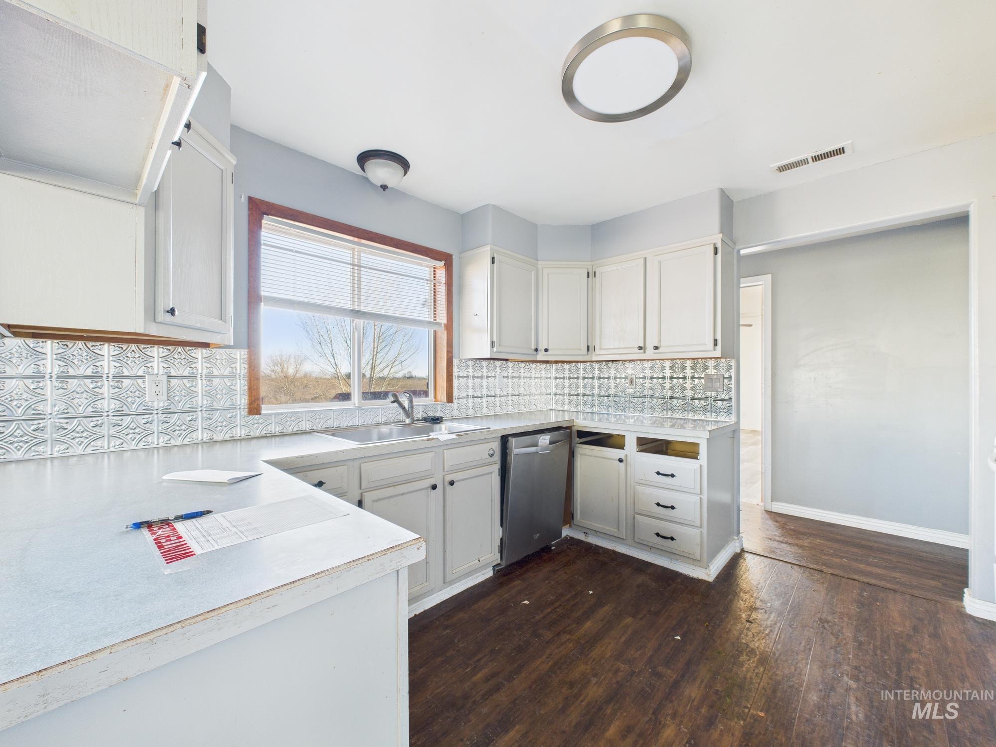 7352 Custer Road Fruitland, ID 83619 - Photo 8 of 43 Kitchen featuring light countertops, dark wood-style floors, stainless steel dishwasher, white cabinetry, and decorative backsplash